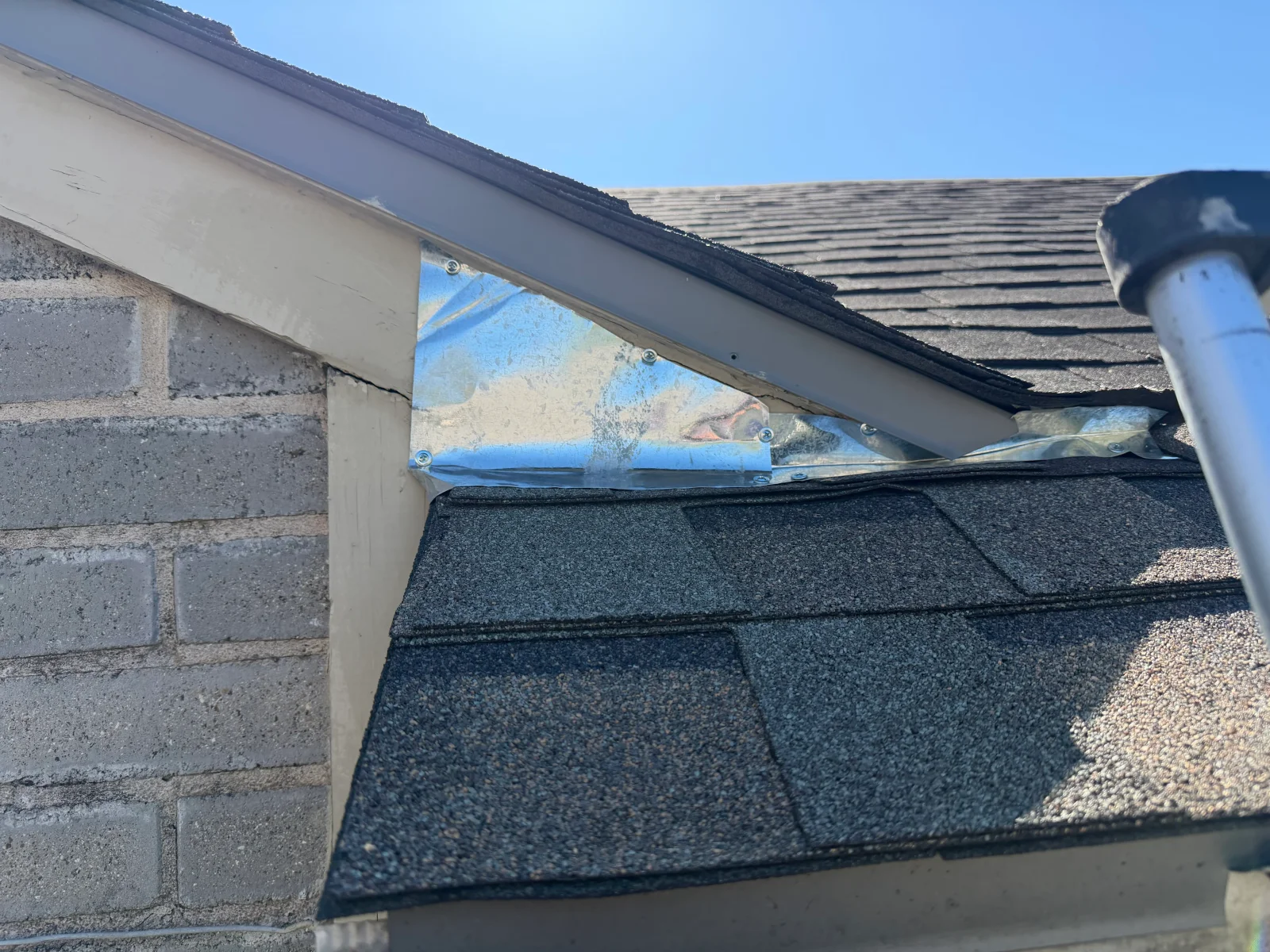 Blue mesh screening installed over roof vents with fasteners, asphalt shingles and brick visible