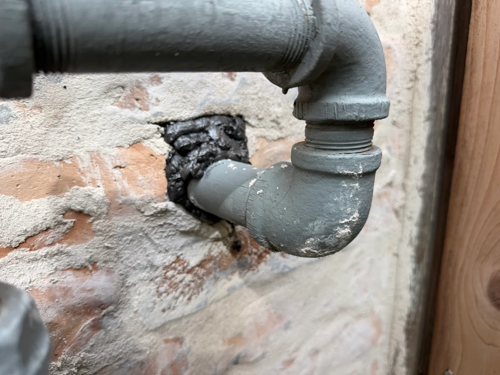 Gray PVC drain pipe with elbow fitting sealed at brick foundation wall