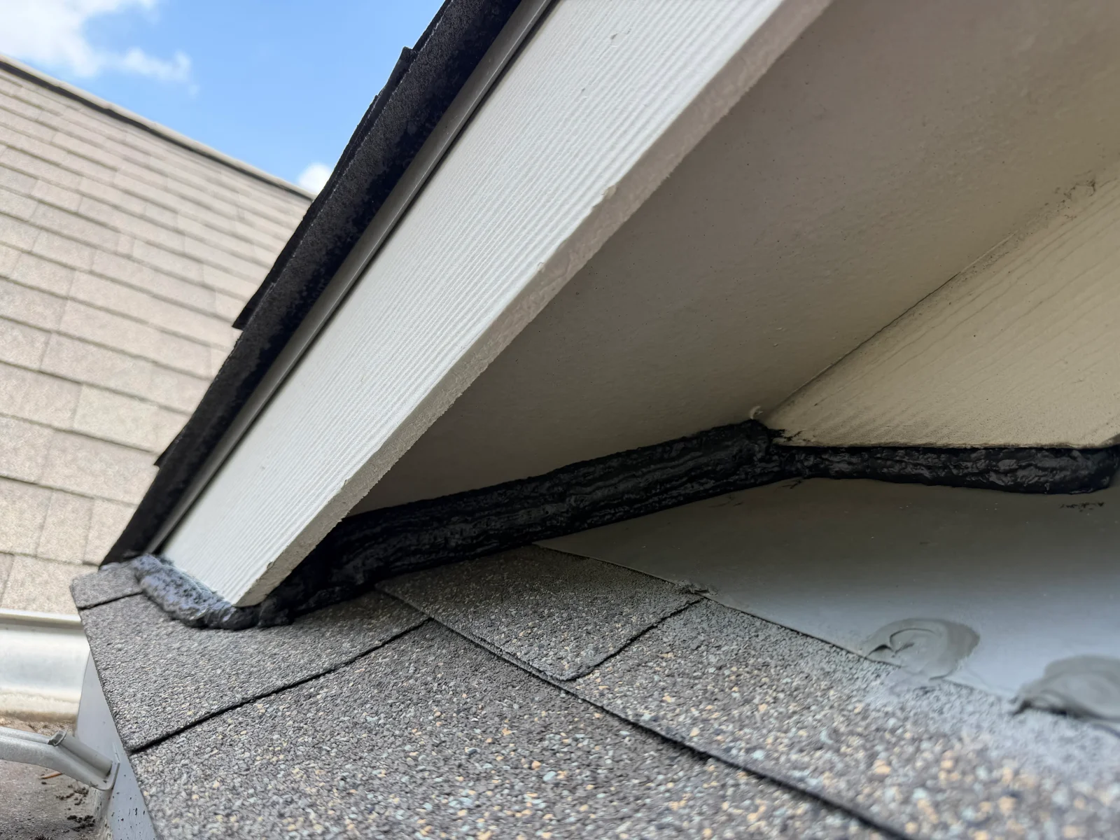 Metal flashing and caulk sealing roof-to-soffit junction on asphalt shingle roof