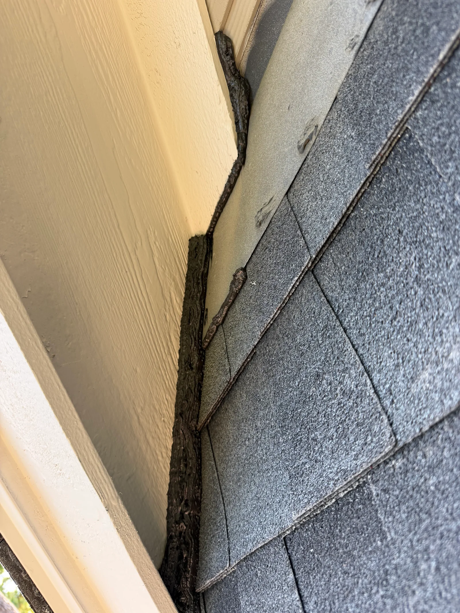 Dark sealant applied to gap between wood siding and asphalt shingles to block rodent entry