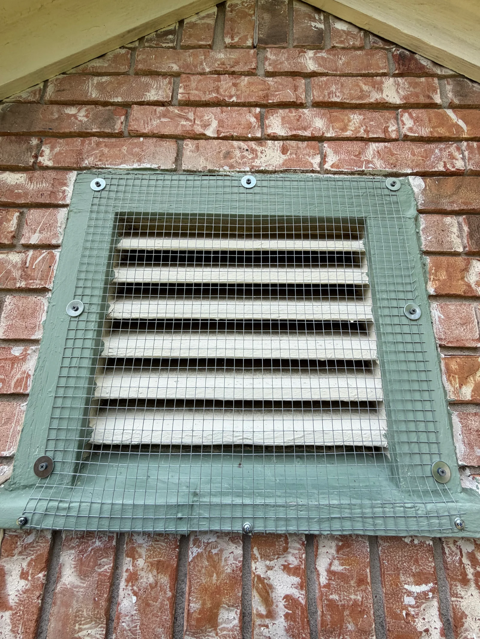 Green mesh exclusion screen installed over brick gable vent with horizontal louvers and stainless steel fasteners