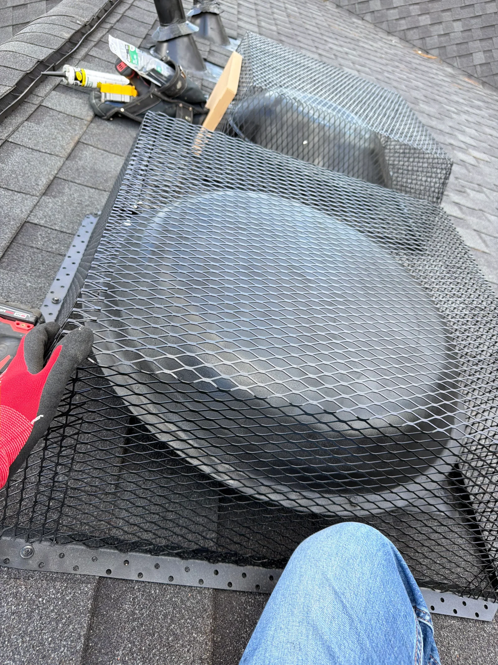 Metal mesh gutter guard installed with riveted brackets on residential roof gutter